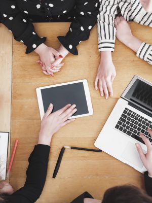 Young business team working together as a group on office desk with multiple electronic devices and paper based tools